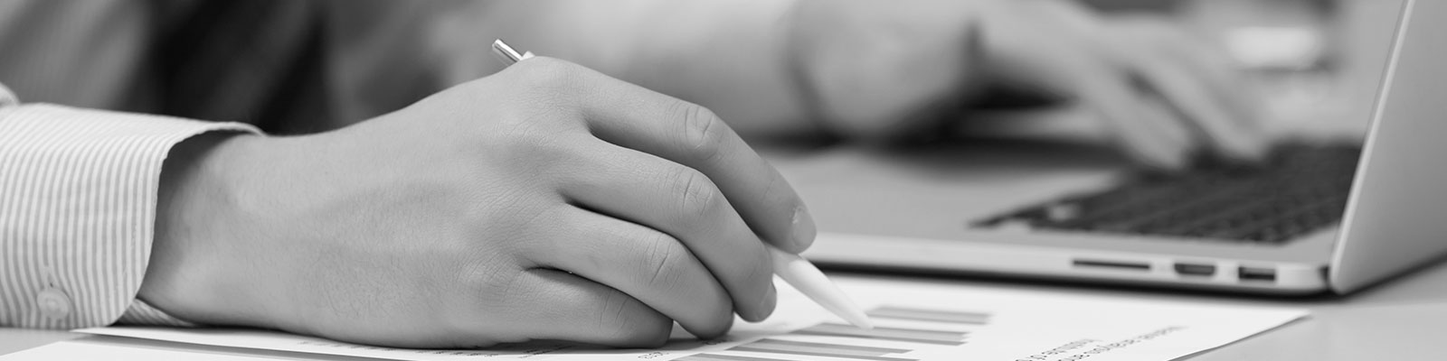 Stock image of a hand holding a pen by a computer